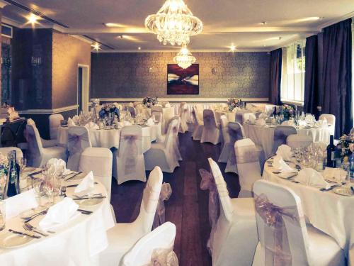 a banquet hall with white tables and chairs and a chandelier at Mercure Milton Keynes Hotel in Milton Keynes