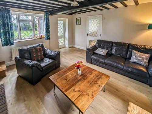 a living room with leather furniture and a wooden table at Pixies Wood Cottage in Ludham
