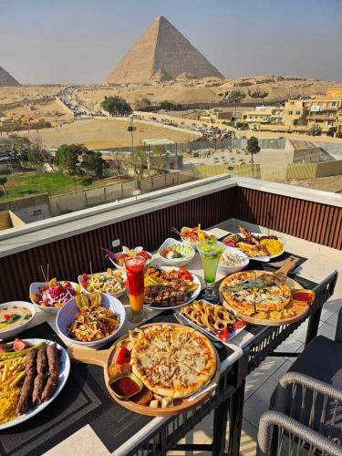 Una mesa con muchos platos de comida y las pirámides. en Pyramids Acme Inn, en Nazlet el-Sîsi