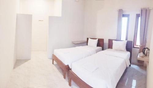 a room with three beds with white sheets and a window at Savira Homestay Labuan Bajo in Labuan Bajo