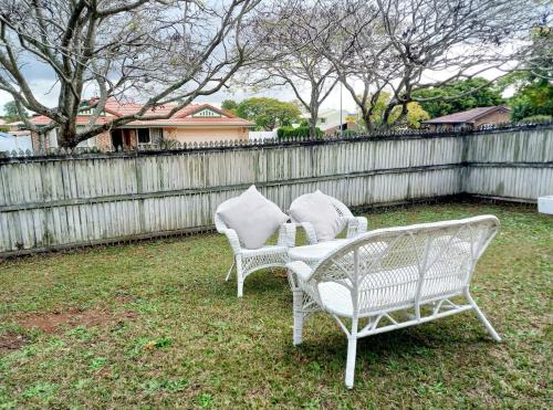 zwei weiße Stühle in einem Garten neben einem Zaun in der Unterkunft 3mins walk to shopping centre city bus airport train station in Brisbane