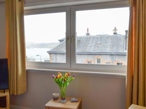 a vase of flowers sitting on a table in front of a window at Finlaggan Apartment in Oban