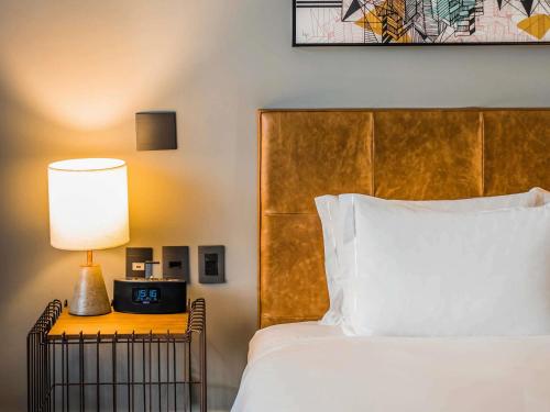 a bed with a lamp and a clock on a night stand at Pullman Sao Paulo Vila Olimpia in Sao Paulo