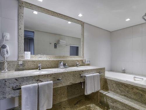 a bathroom with two sinks and a tub and a large mirror at Caesar Business Belo Horizonte Belvedere in Belo Horizonte