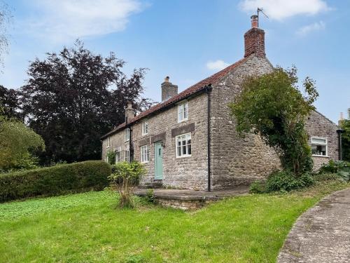 an old stone house with a green door in a field at Lawns Cottage in Helmsley