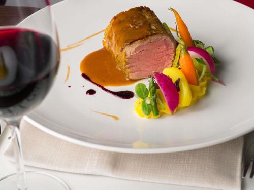 a piece of meat and vegetables on a plate with a glass of wine at Novotel Caserta Sud in Caserta