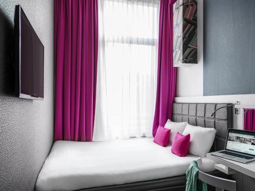 a bedroom with a bed with pink curtains and a laptop at ibis Styles Amsterdam Amstel in Amsterdam