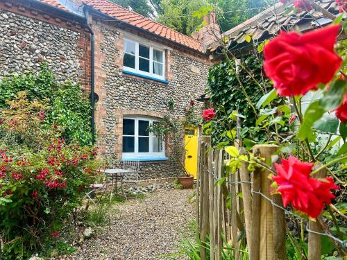 a brick house with a fence and red roses at Forge Cottage in Stiffkey