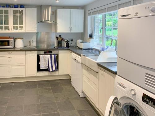 a kitchen with white cabinets and a washer and dryer at Castle Cottage in Ruan Lanihorne