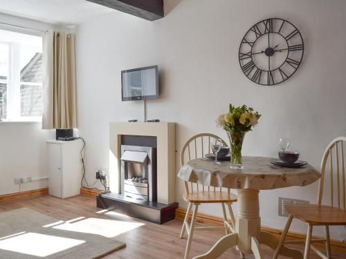 a living room with a table and a clock on the wall at Weavers Houses - Uk12796 in Hayfield