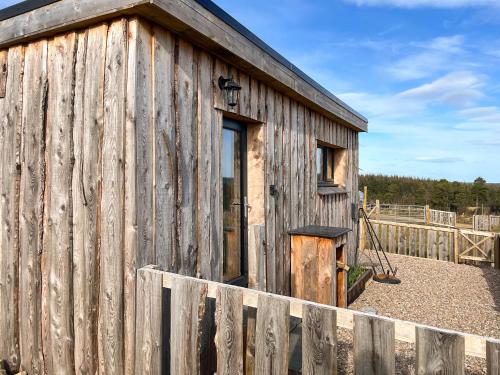 a wooden building with a door and a fence at Honeysuckle Bale Cabin - Uk49073 in Ballindalloch