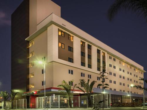 a large white building with palm trees in front of it at Ibis Porto Alegre Assis Brasil in Porto Alegre