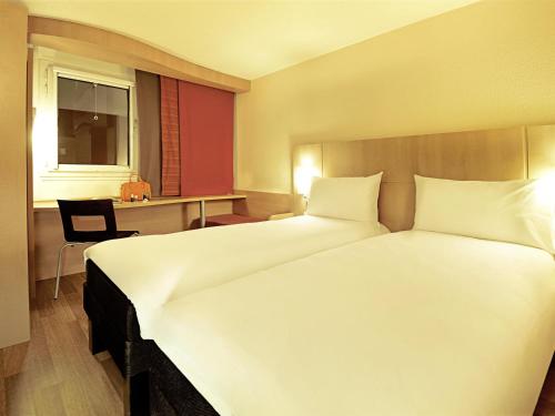 a bedroom with a large white bed and a desk at Ibis Porto Alegre Assis Brasil in Porto Alegre