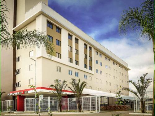 a large white building with palm trees in front of it at Ibis Porto Alegre Assis Brasil in Porto Alegre