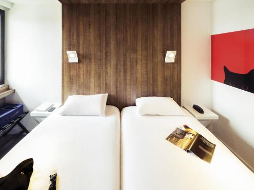 two beds in a hotel room with avertisement for at ibis Styles Niort Poitou Charentes in Vouillé