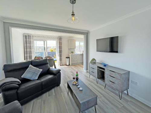 a living room with a black couch and a flat screen tv at Driftwood Cottage in Portpatrick