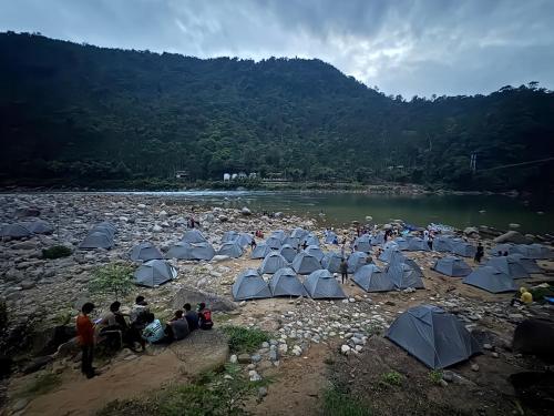 a group of people sitting around tents on a river at shnongpdeng tents stay in Dawki