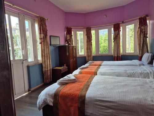 2 bedden in een slaapkamer met paarse muren en ramen bij Hotel Fishtail Villa in Pokhara