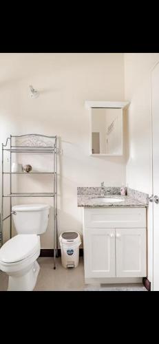 a white bathroom with a toilet and a sink at Breezy Bungalow Gated 2BR w Pool WiFi in Old Harbour