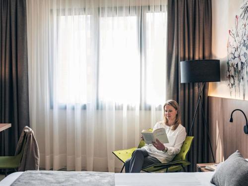 a woman sitting in a chair reading a book in a hotel room at Mercure Barcelona Condor in Barcelona