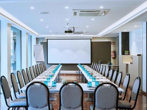 a conference room with a long table with chairs and a projection screen at Mercure Barcelona Condor in Barcelona