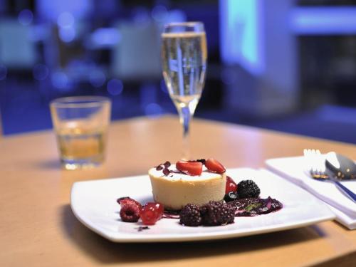 a piece of cake and berries on a plate with a glass at Mercure North Melbourne in Melbourne