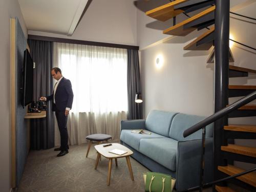 a man in a suit standing in a living room at Novotel Brussels Centre Midi in Brussels