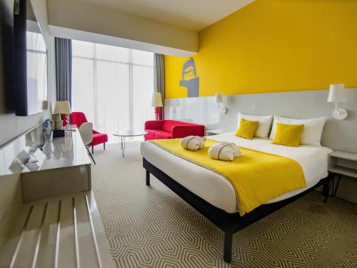 a hotel room with a large bed with a yellow wall at Ibis Styles Wroclaw Centrum in Wrocław
