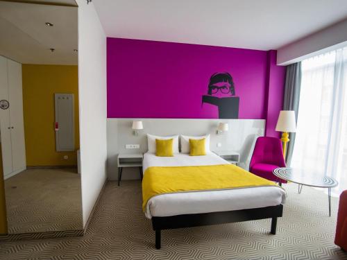 a hotel room with a bed and a purple wall at Ibis Styles Wroclaw Centrum in Wrocław