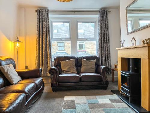 a living room with a leather couch and a fireplace at Hollybush Cottage in Buxton