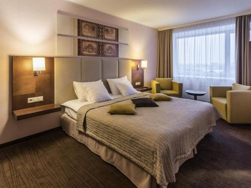 a hotel room with a large bed and a chair at Mercure Marijampole in Marijampolė