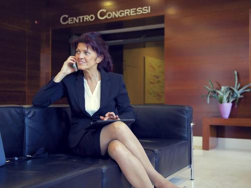 a woman sitting on a couch talking on a cell phone at Mercure Genova San Biagio in Genova