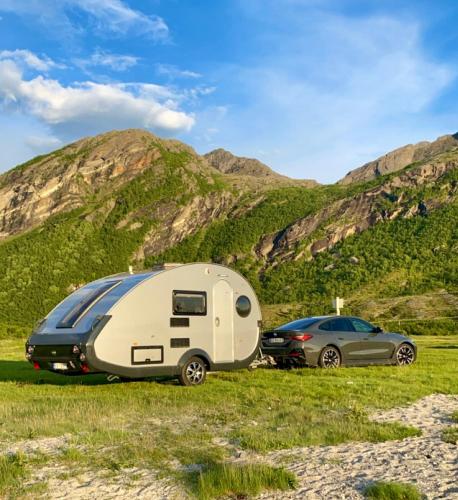 a caravan and a car parked in a field with mountains at Enkel, romslig og kul campingvogn in Moskenes