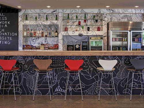 a bar with red stools in front of a mural at ibis Londrina Shopping in Londrina