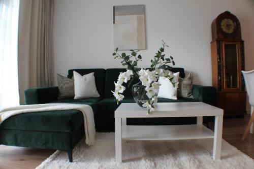 a living room with a green couch and a table with flowers at VESTA Apartamenty M52 Free parking in Szczecin