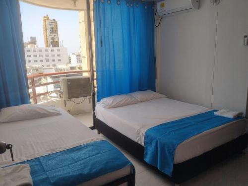 2 Betten in einem Zimmer mit blauen Vorhängen und einem Fenster in der Unterkunft Apartamento Rodadero Con Piscinas y Cancha de Tennis in Rodadero