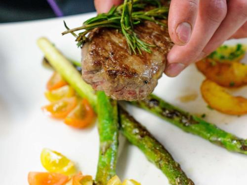 a person holding a piece of meat on a plate with asparagus at Mercure Hotel Dortmund Centrum in Dortmund