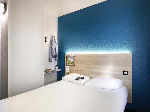 a white bed in a room with a blue wall at hotelF1 Calais Coquelles in Coquelles
