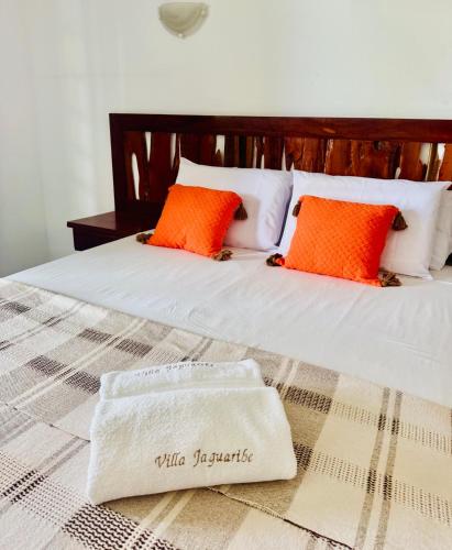 a bed with orange and white pillows and a towel at Villa Jaguaribe in Fortim