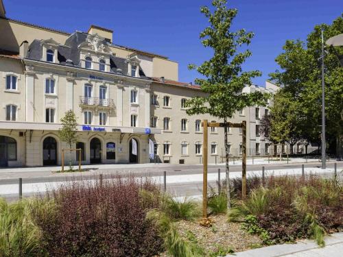 a building with a tree in front of a street at ibis budget Le Puy En Velay in Le Puy en Velay