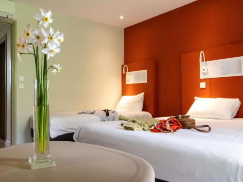 a vase of flowers sitting on a table with two beds at ibis budget Le Puy En Velay in Le Puy en Velay