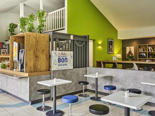 a restaurant with tables and stools in front of a counter at Ibis Budget Versailles Coignieres in Coignières