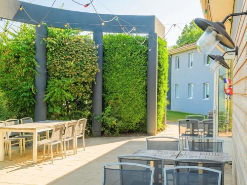 a patio with tables and chairs and a green hedge at greet hôtel Annecy Cran-Gevrier by Accor in Annecy