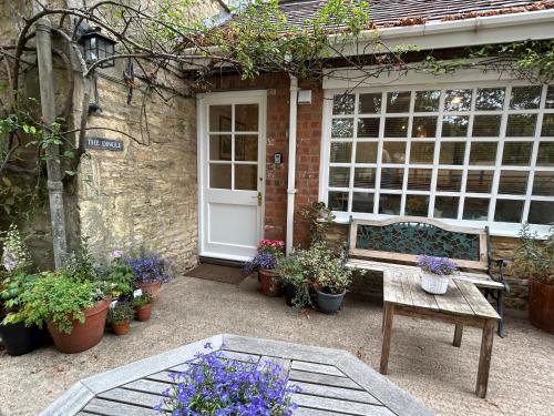 eine Bank, die vor einem Haus mit Pflanzen sitzt in der Unterkunft Four Seasons Cottage - in the Cotswolds in Tewkesbury