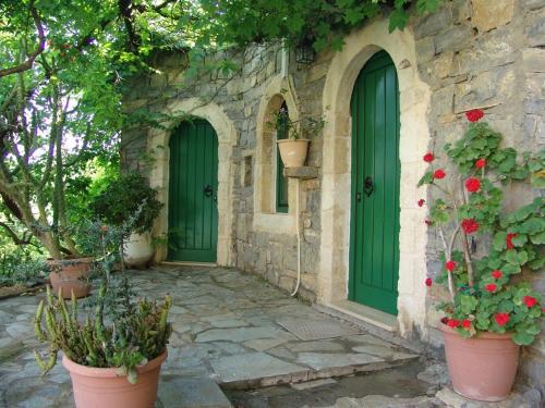 a stone house with green doors and flowers in pots at Arolithos Traditional Village Hotel in Tílisos