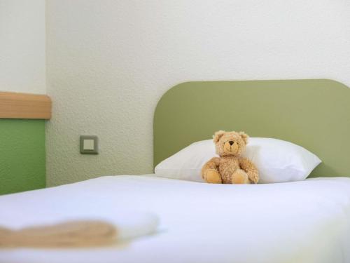 a teddy bear sitting on top of a bed at ibis budget Narbonne Sud A9/A61 in Narbonne