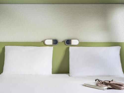 two clocks on the head of a bed with two pillows at ibis budget Paris Porte de Bercy in Charenton-le-Pont