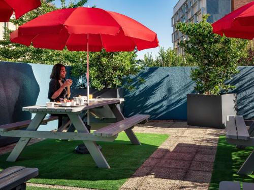 a woman sitting at a picnic table with a red umbrella at ibis budget Paris Porte d'Aubervilliers in Aubervilliers