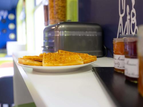 a plate of waffles on a counter next to a toaster at ibis budget Besançon Centre Gare in Besançon