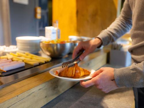 a person holding a plate of food with a fork and knife at ibis budget Besançon Centre Gare in Besançon